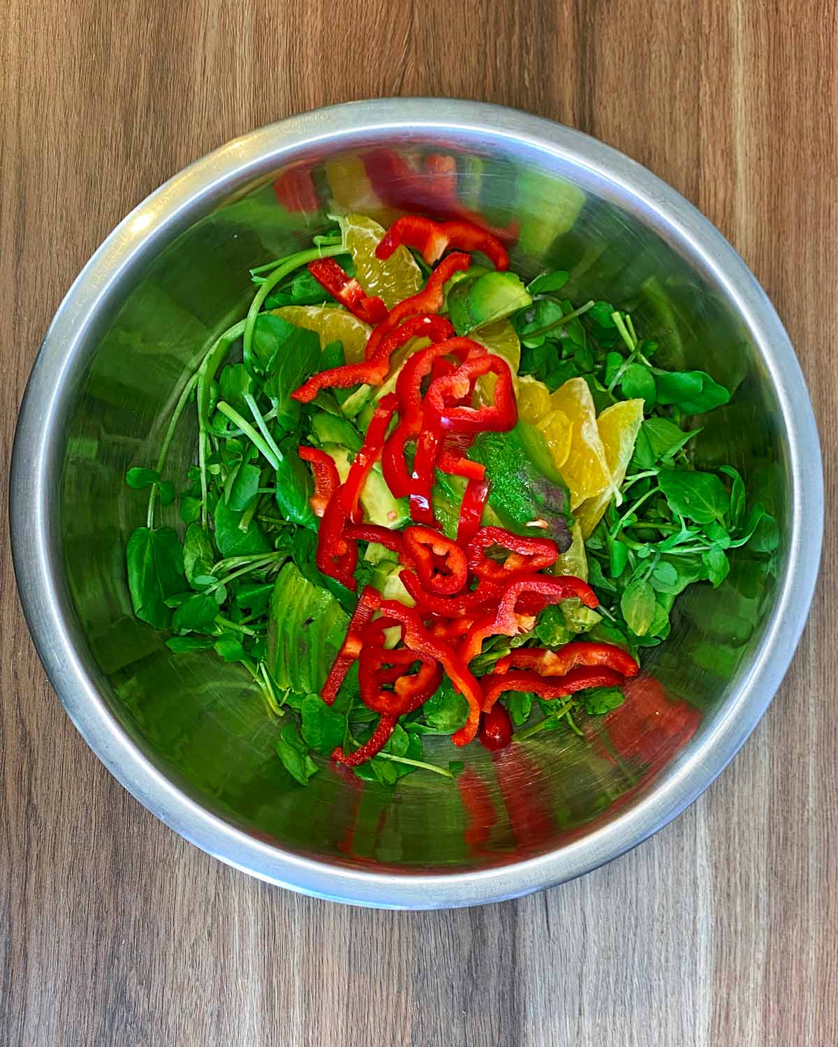 Watercress, sliced avocado, sliced orange and sliced red pepper in a large bowl.