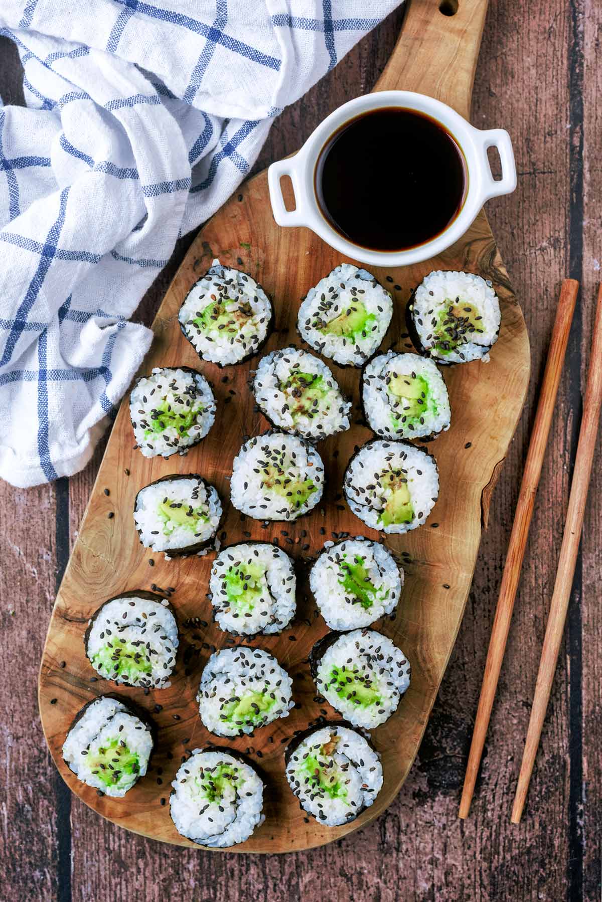 Avocado sushi rolls on a wooden board with a small bowl of soy sauce.
