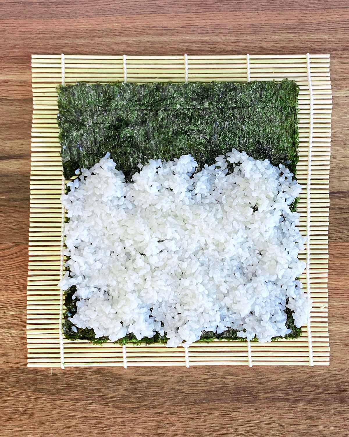 A sushi rolling mat with a sheet of nori with sushi rice on it.