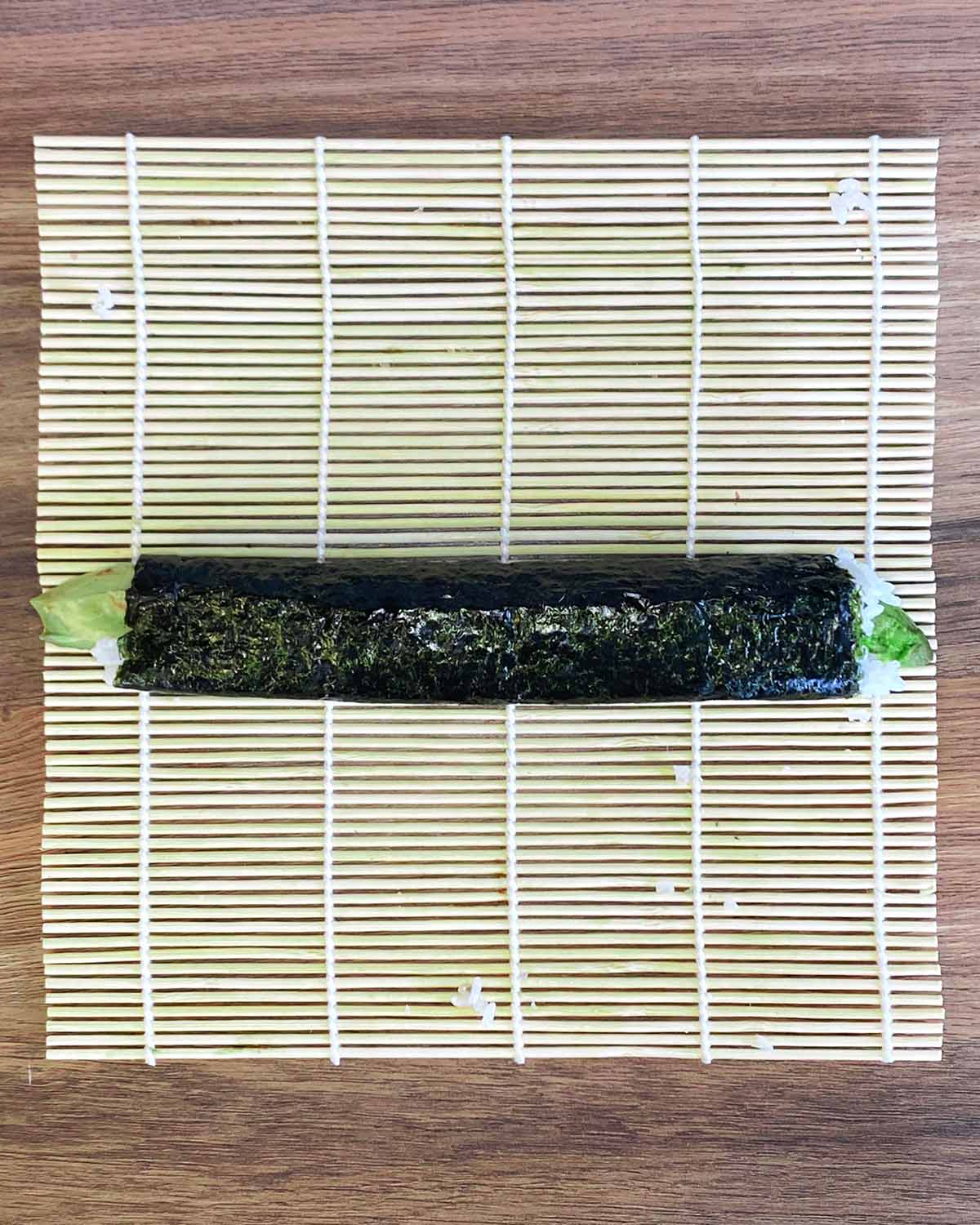 A full sushi roll on a bamboo mat.