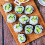 Ten pieces of cucumber maki on a wooden serving board.