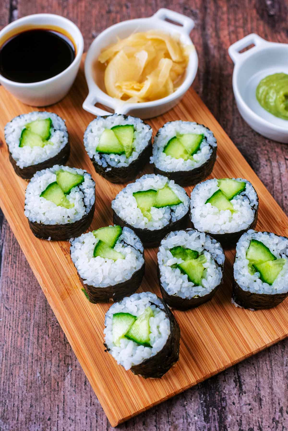 Cucumber sushi maki on a board with a small bowl of soy sauce and pickled ginger.
