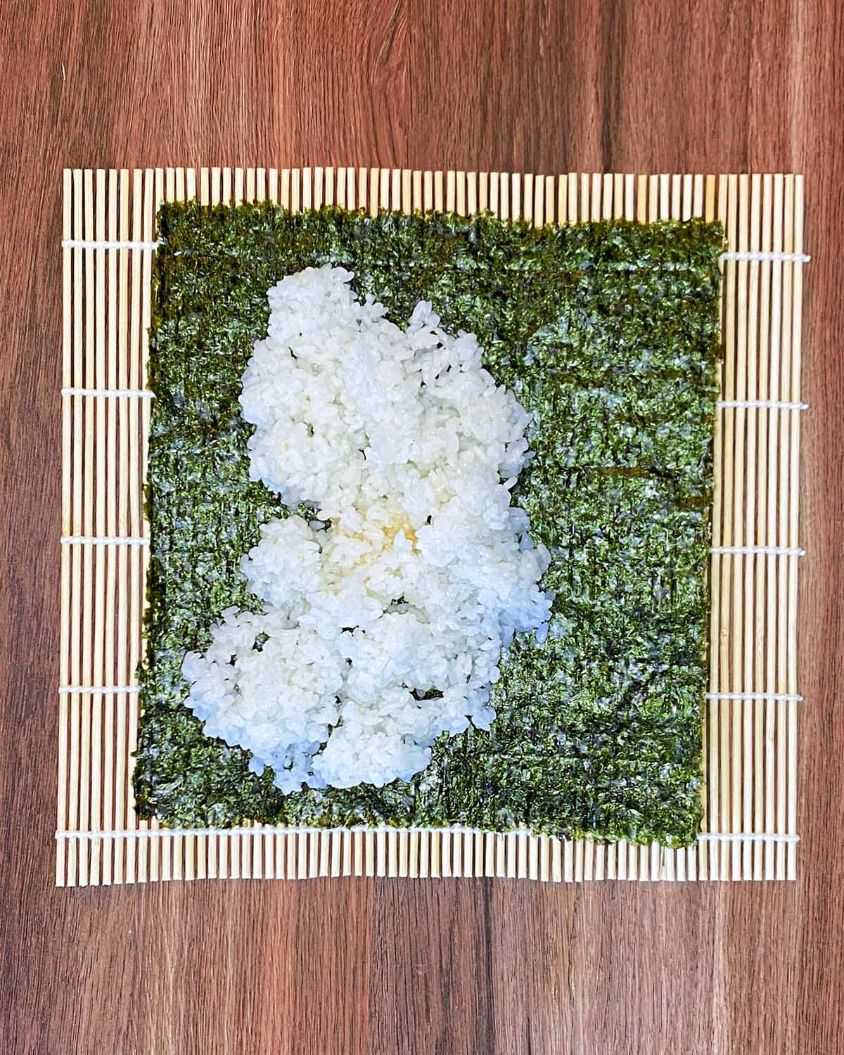 A bamboo rolling mat with nori and sushi rice on it.