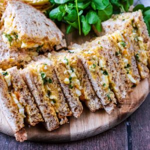 A row of egg and cress sandwiches on a wooden board.