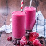 Two glasses of frozen fruit smoothie next to some frozen berries.