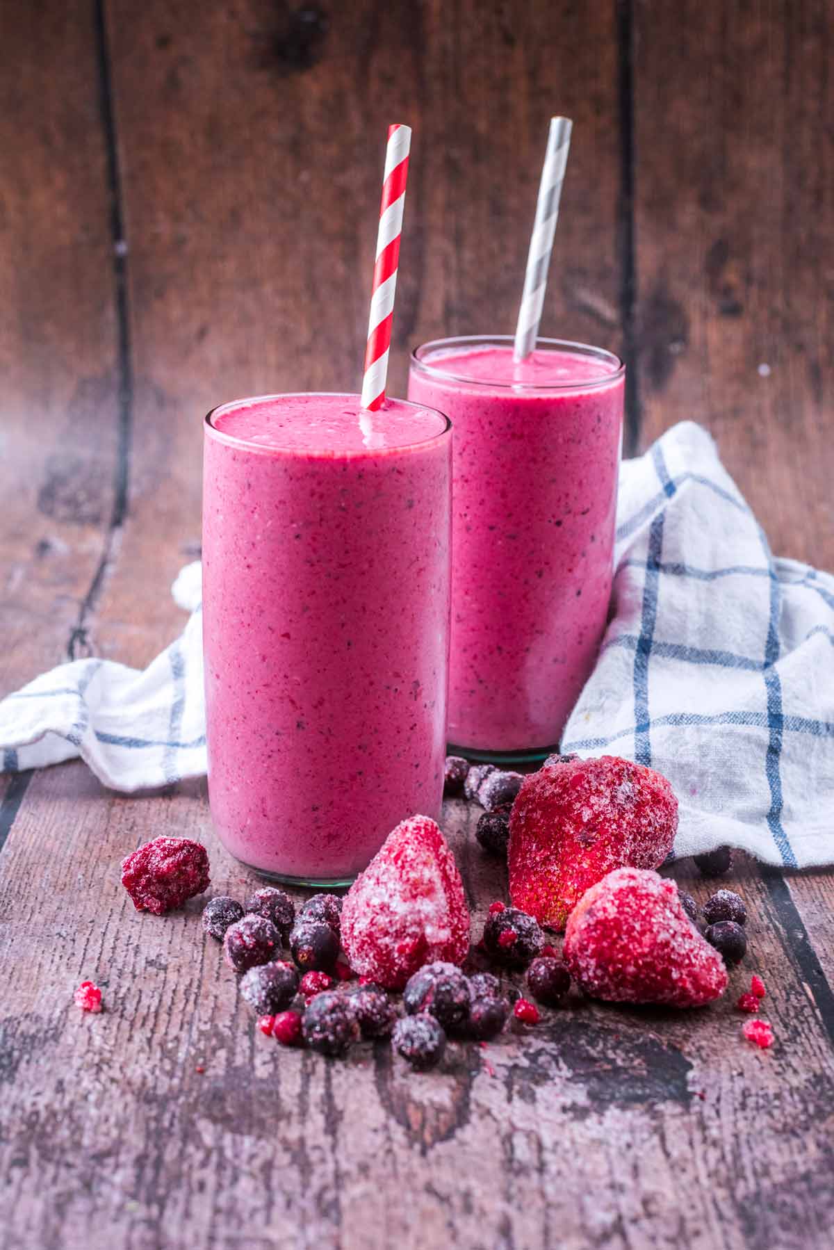 Two glasses of pink coloured smoothie with striped drinking straws.