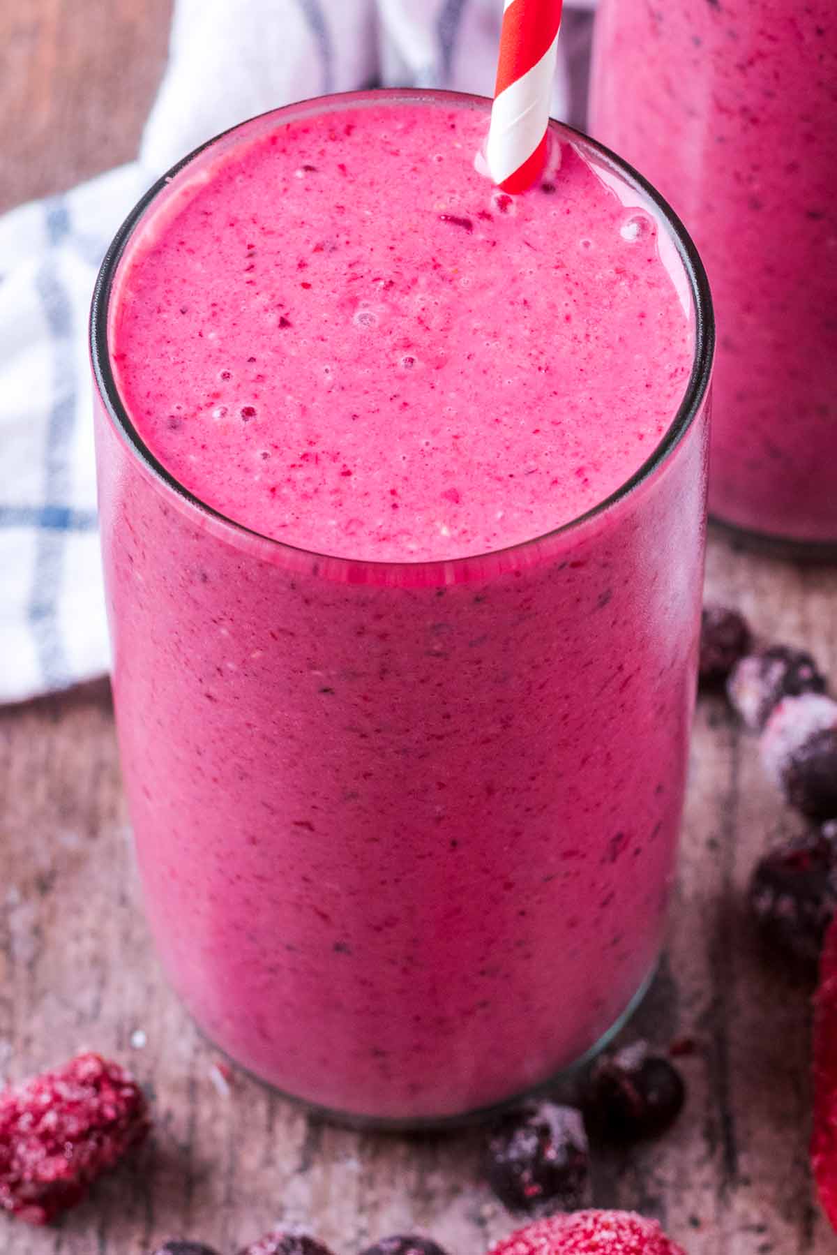 A pink fruit smoothie with a red and white striped drinking straw.