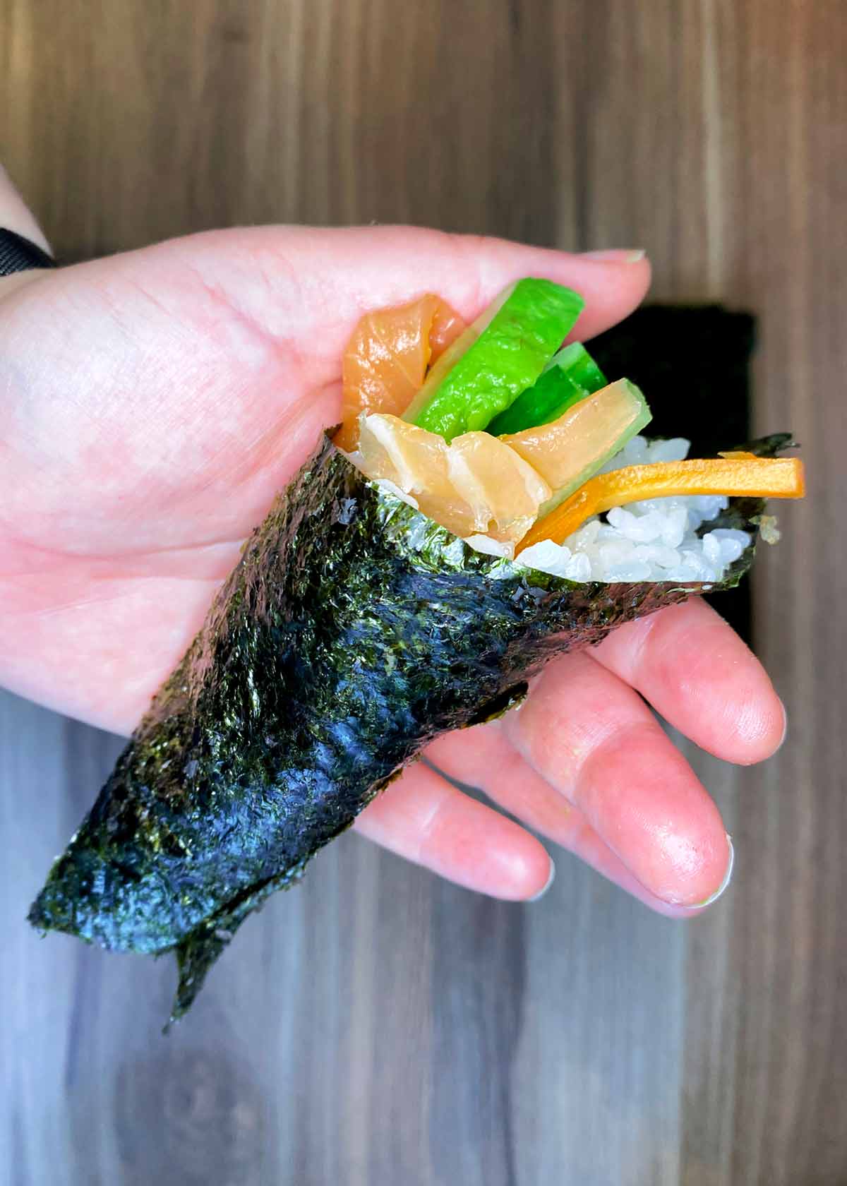 A hand holding up sushi hand roll.