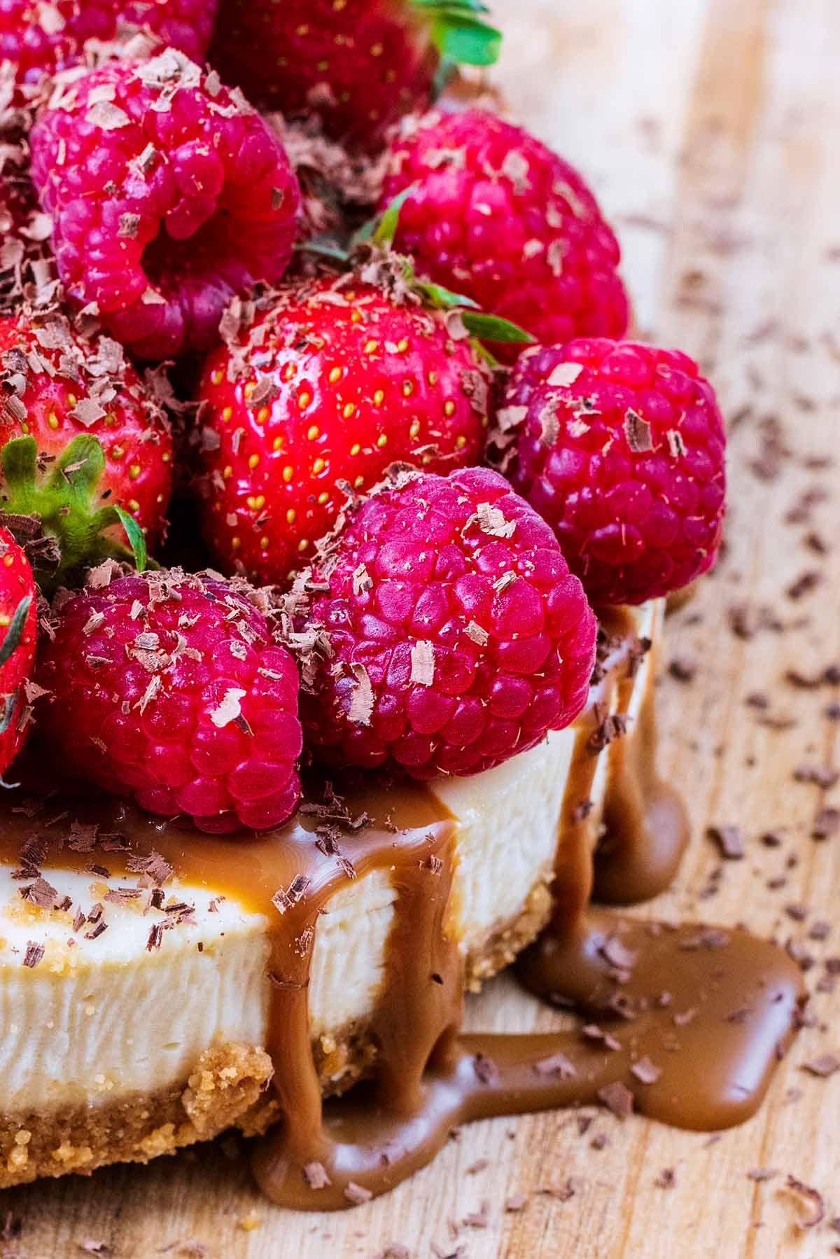 Strawberries and raspberries on top of a cheesecake with caramel sauce dripping down the side.