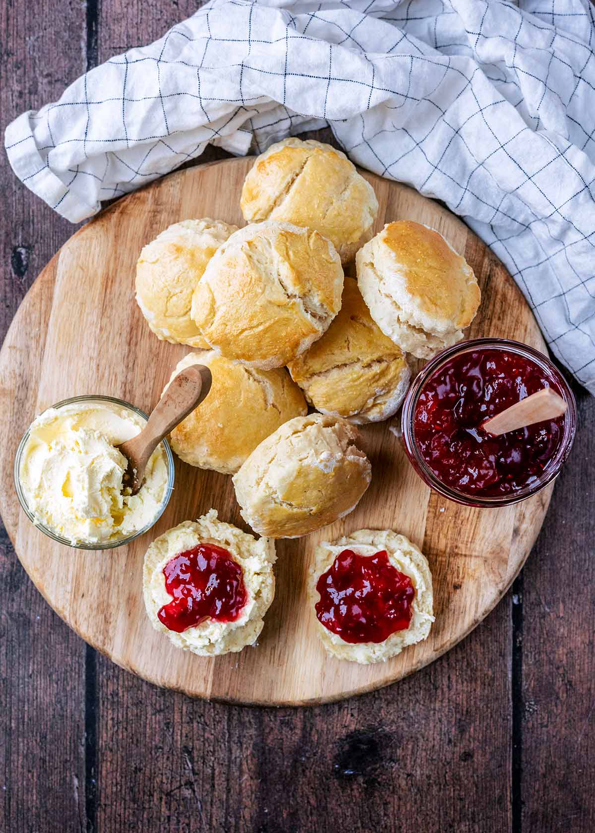 Eight scones on a board, one is cut open with cream and jam on it.