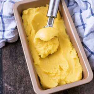 A rectangular tin full of mango sorbet with some being scooped out.