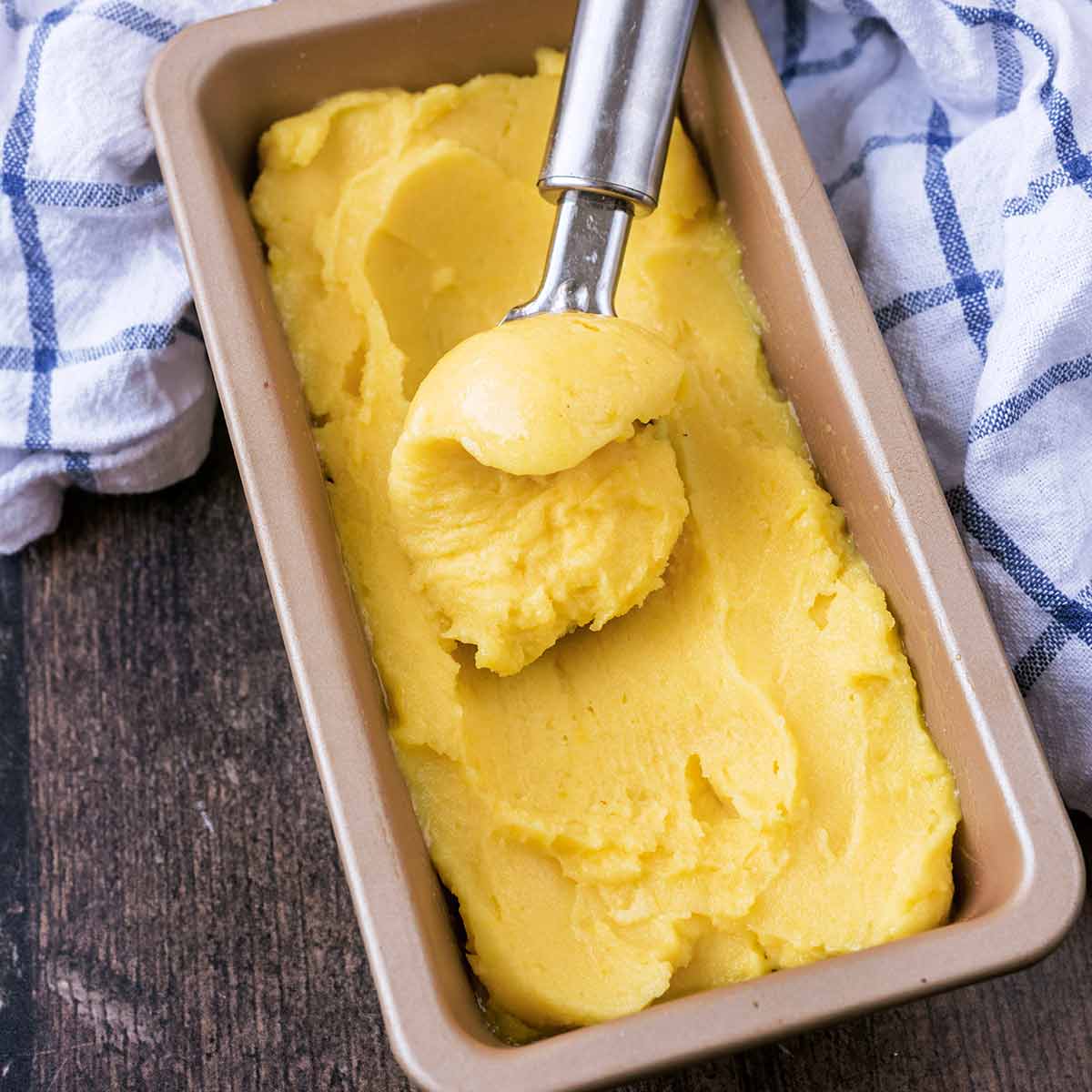 A rectangular tin full of mango sorbet with some being scooped out.