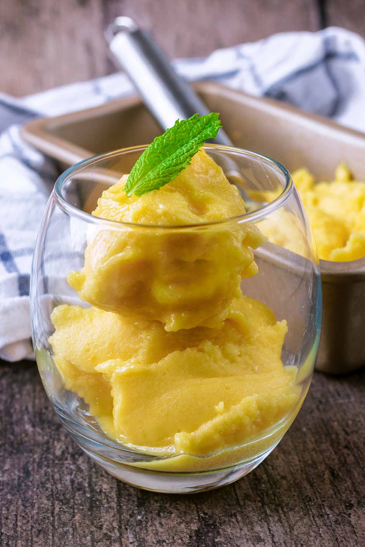 A serving glass containing mango sorbet topped with a mint leaf.