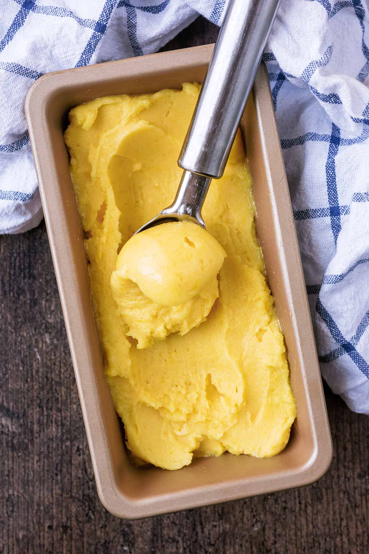 A tub of sorbet with an ice cream scoop scooping some out.