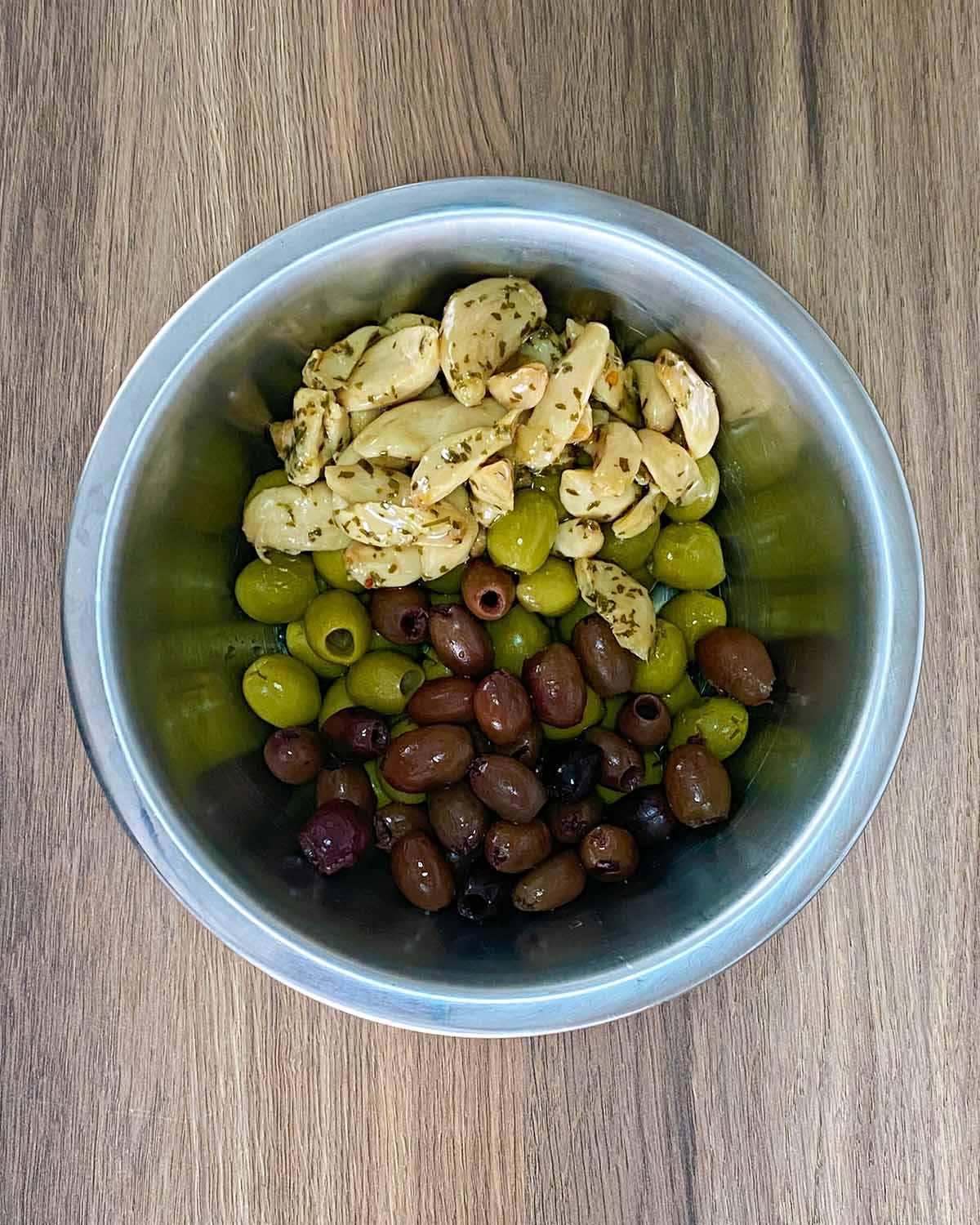 A mixing bowl containing green olives, black olives and garlic cloves.