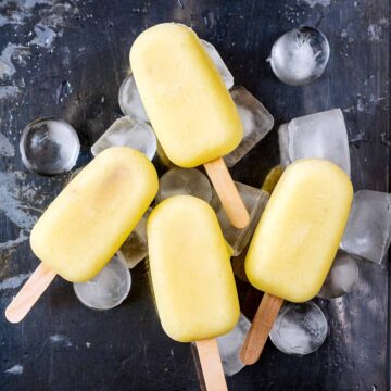 Four pineapple ice lollies on a bed of ice.