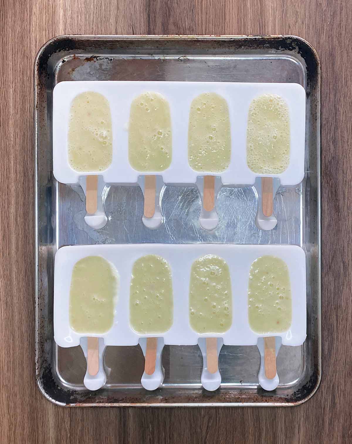 Two lolly moulds of four lollies each with pineapple and coconut milk blend in them.