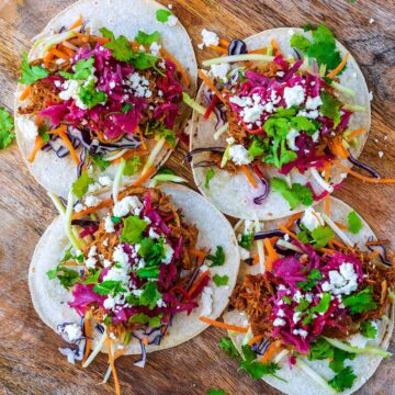 Four pulled pork tacos on a wooden surface.