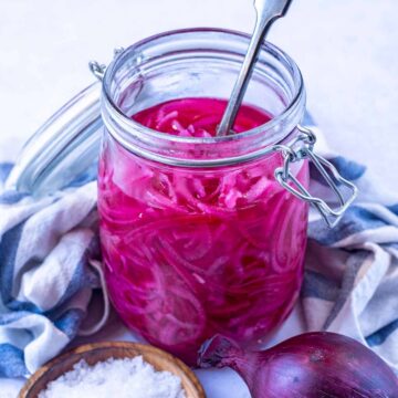 A jar of pickled red onions with a fork in it.