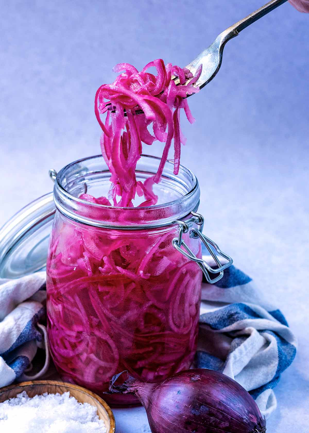 A fork lifting some slices of red onion out of a glass jar.