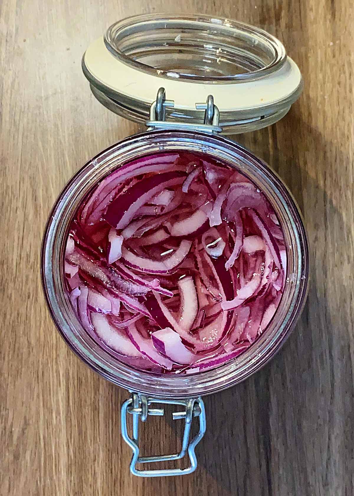 A glass jar containing sliced red onions and pickling liquid.