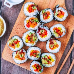 Thirteen pieces of rainbow sushi on a wooden serving board.