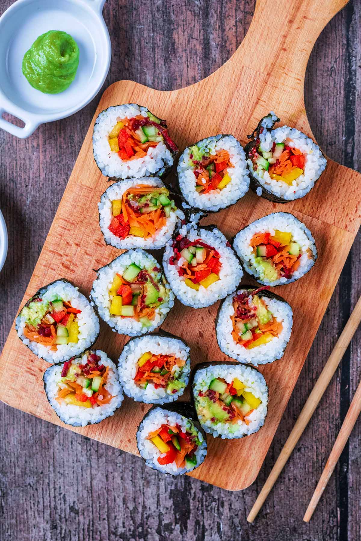 Vegetable filled sushi rolls on a serving board next to some chopsticks and wasabi.