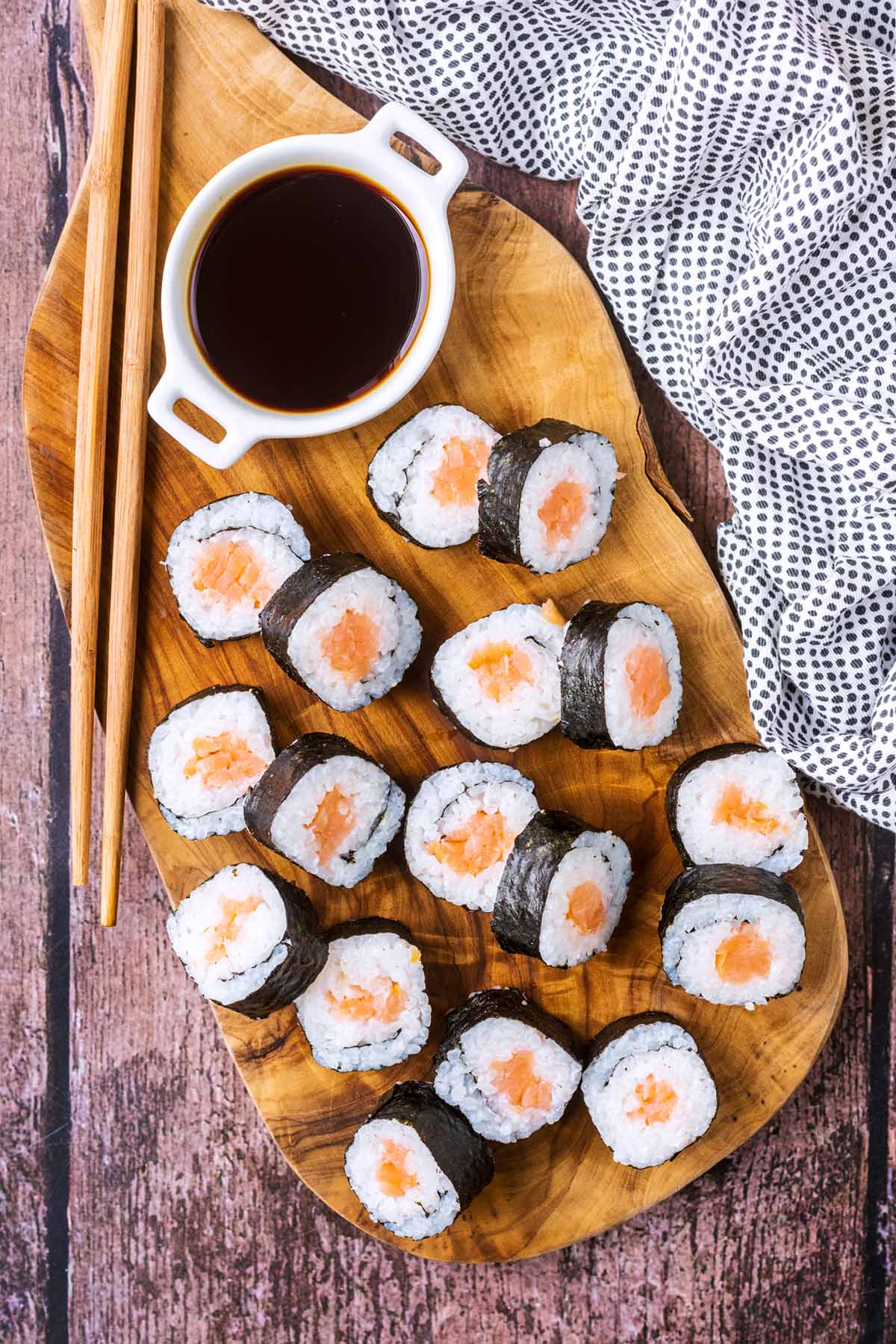 Seventeen pieces of salmon sushi on a wooden serving board.