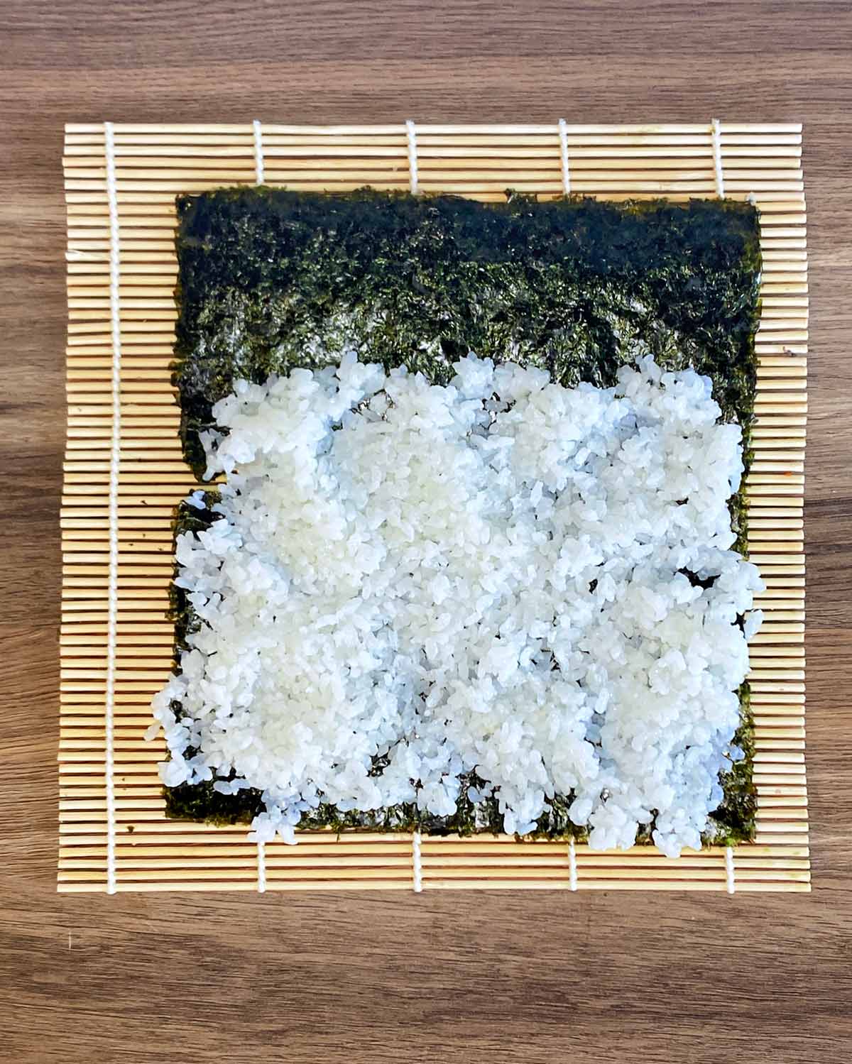 A sheet of nori with sushi rice spread three quarters over it.