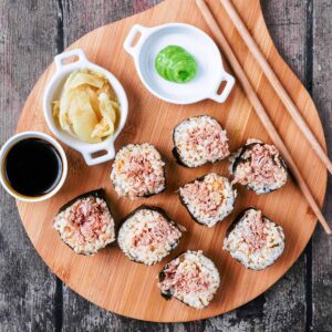 Eight spicy tuna rolls on a board with soy sauce, wasabi and pickled ginger.