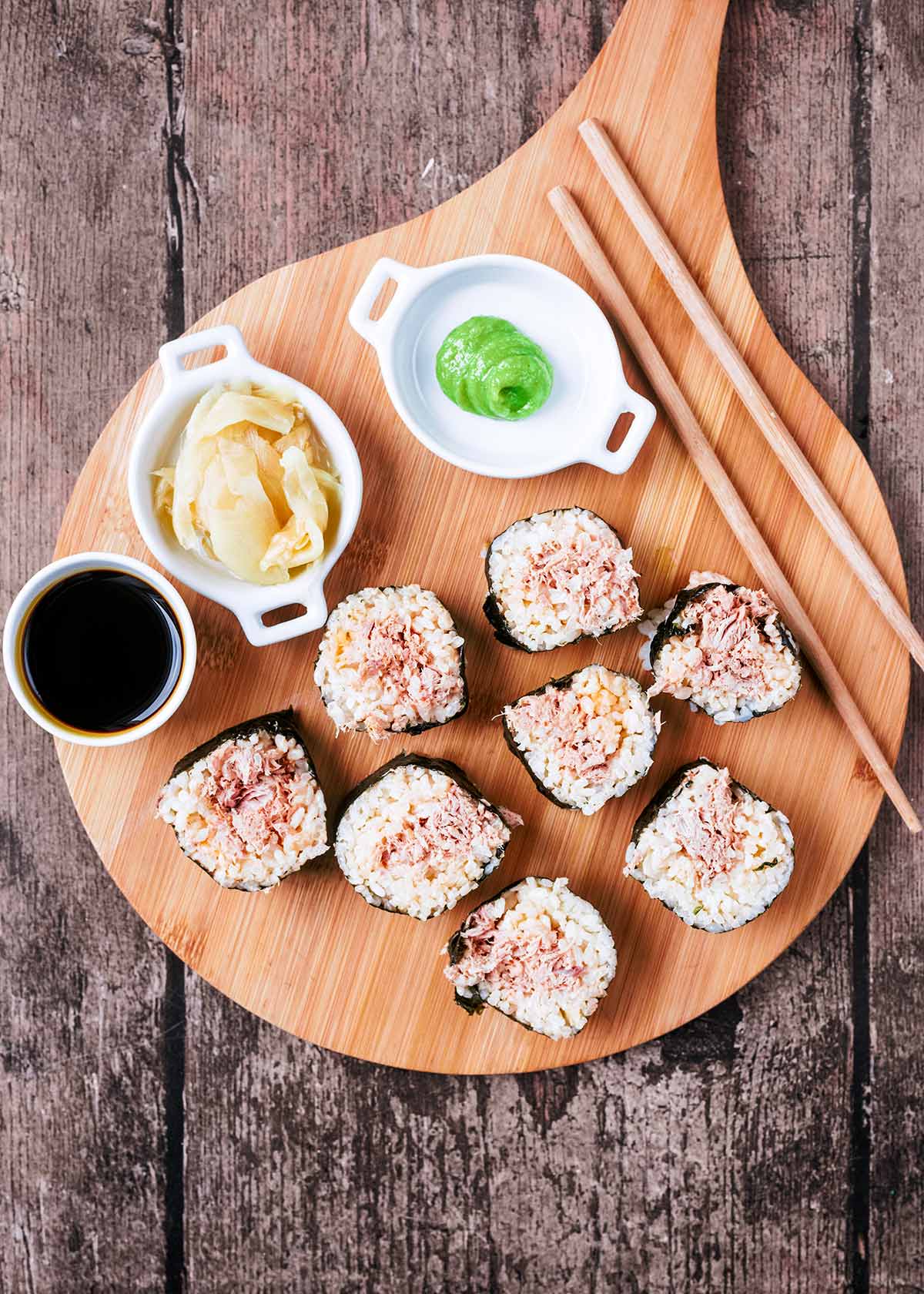 Eight pieces of tuna sushi on a board with soy sauce, wasabi and ginger.