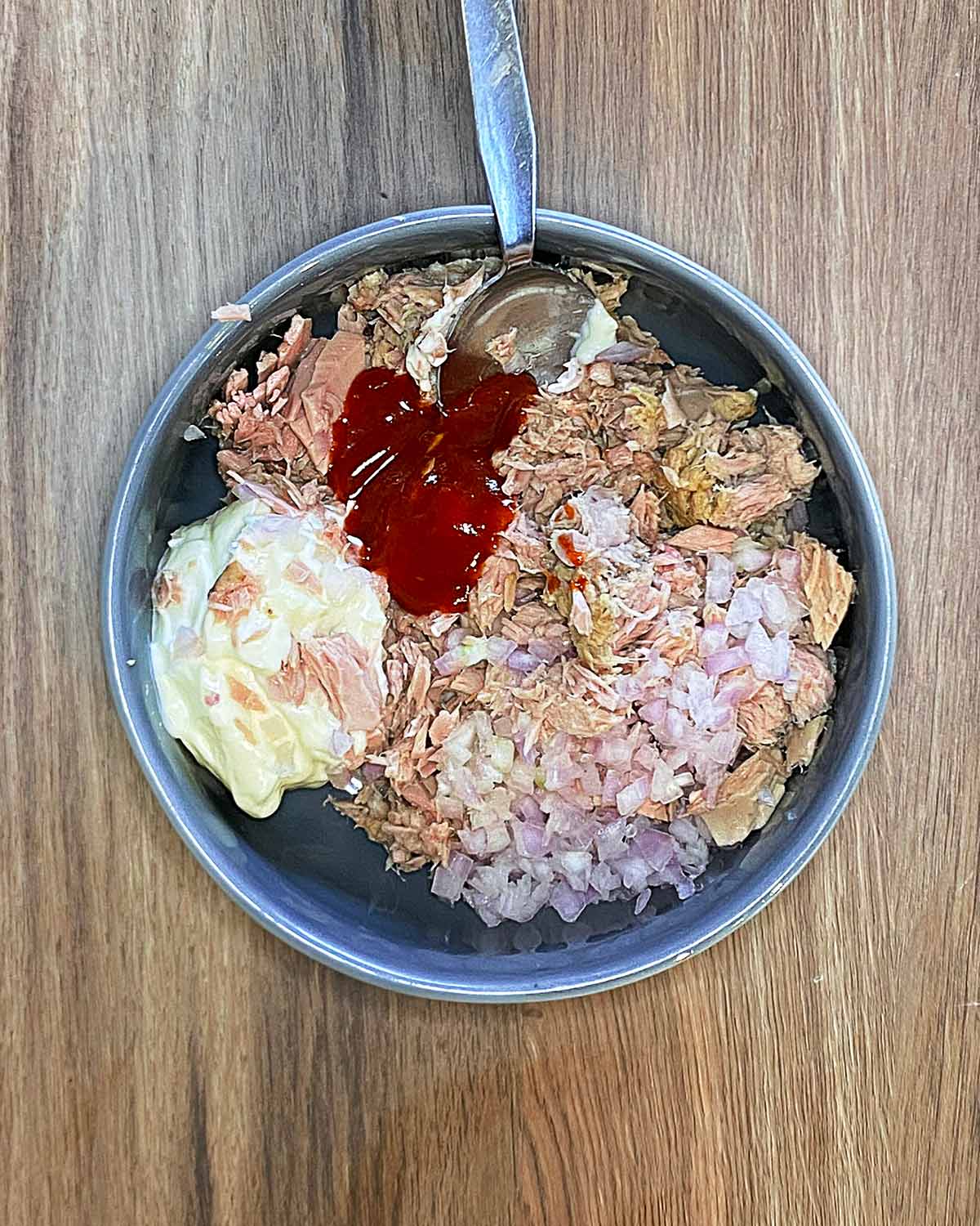 A bowl containing tuna, diced onion, mayonnaise and chilli sauce.
