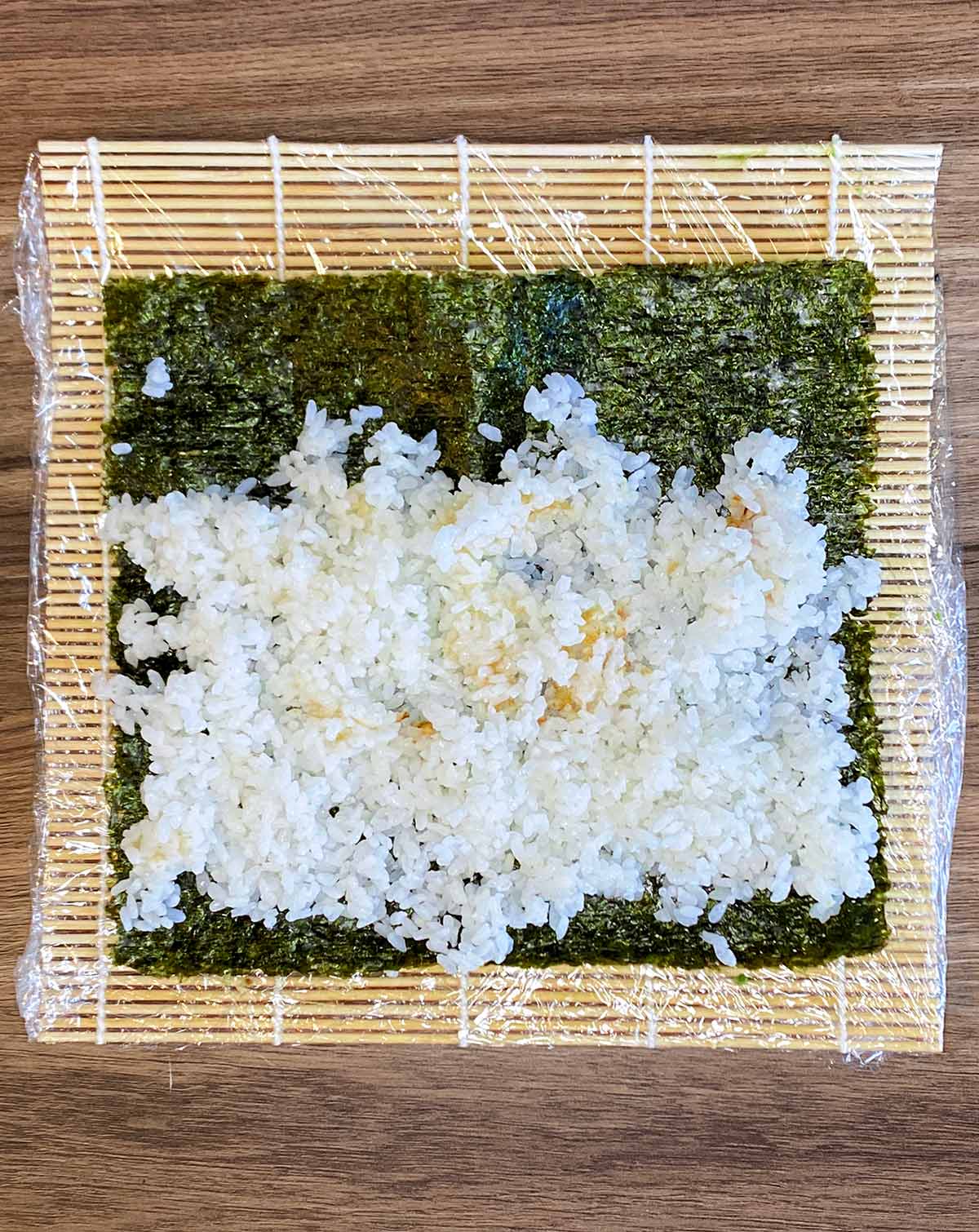 A sheet of nori on a rolling mat with sushi rice on it.