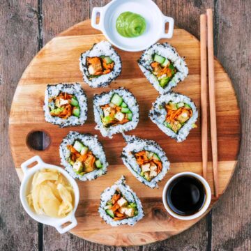 Eight pieces of vegan sushi on a round wooden board.