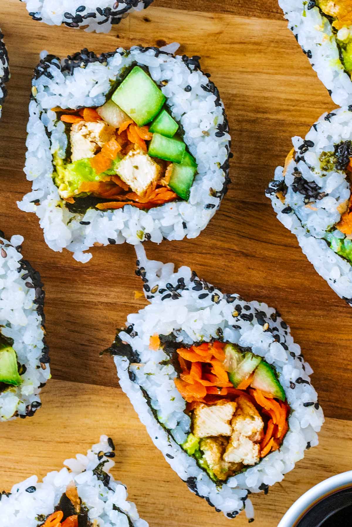 Two vegan sushi rolls on a wooden surface.