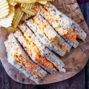 Four triangular cheese savoury sandwiches on a wooden board.