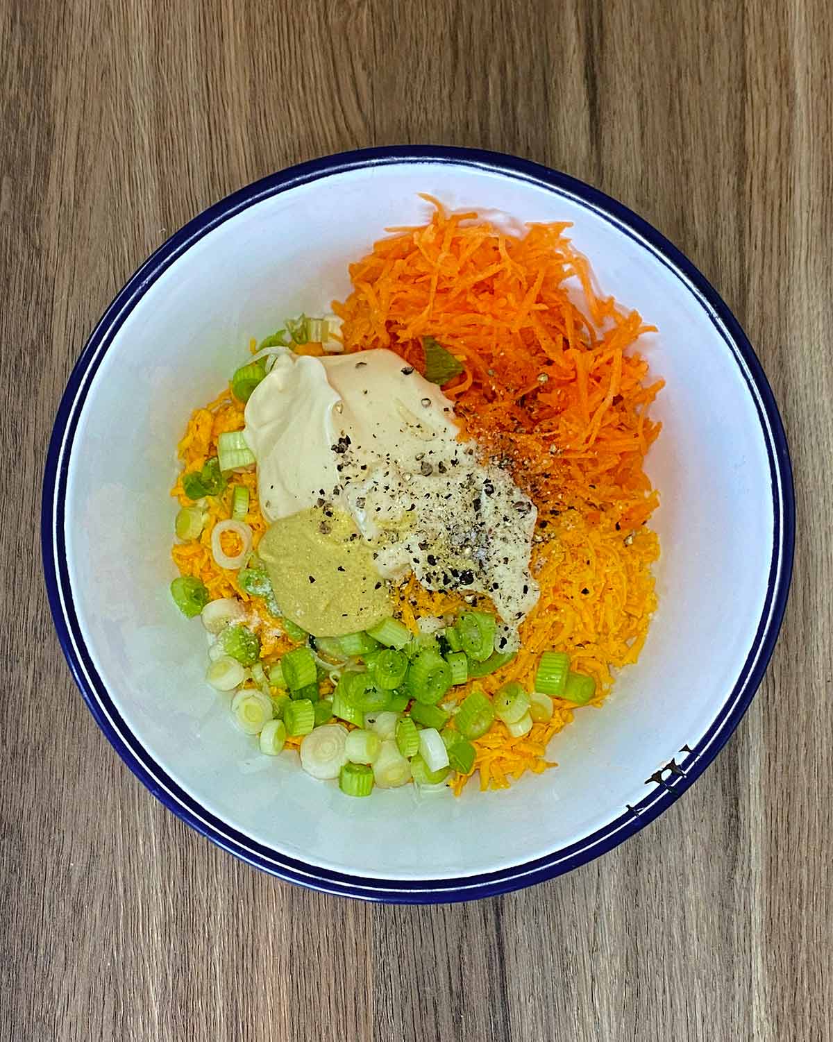 Grated cheese, carrot, spring onions, mayo, mustard and seasoning in a mixing bowl.