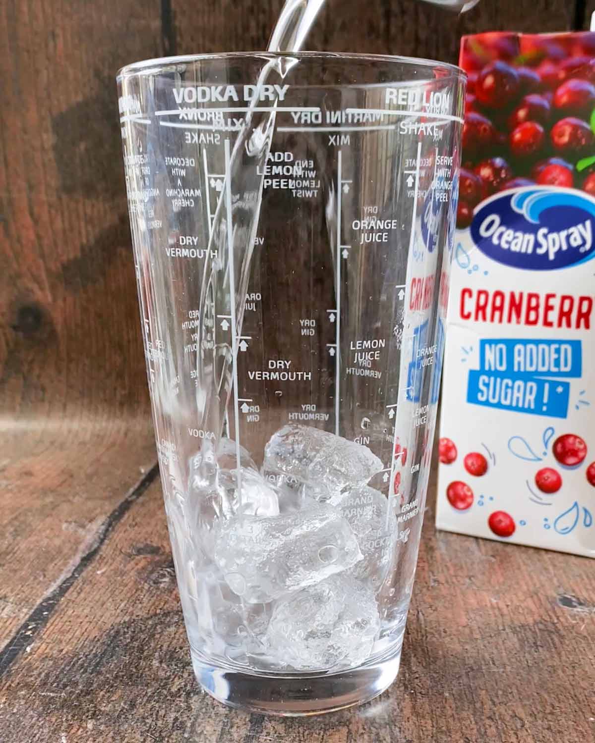 A cocktail shaker with ice cubes and vodka in it.