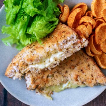 Air fryer cheese toastie on a plate with crisps and lettuce leaves.