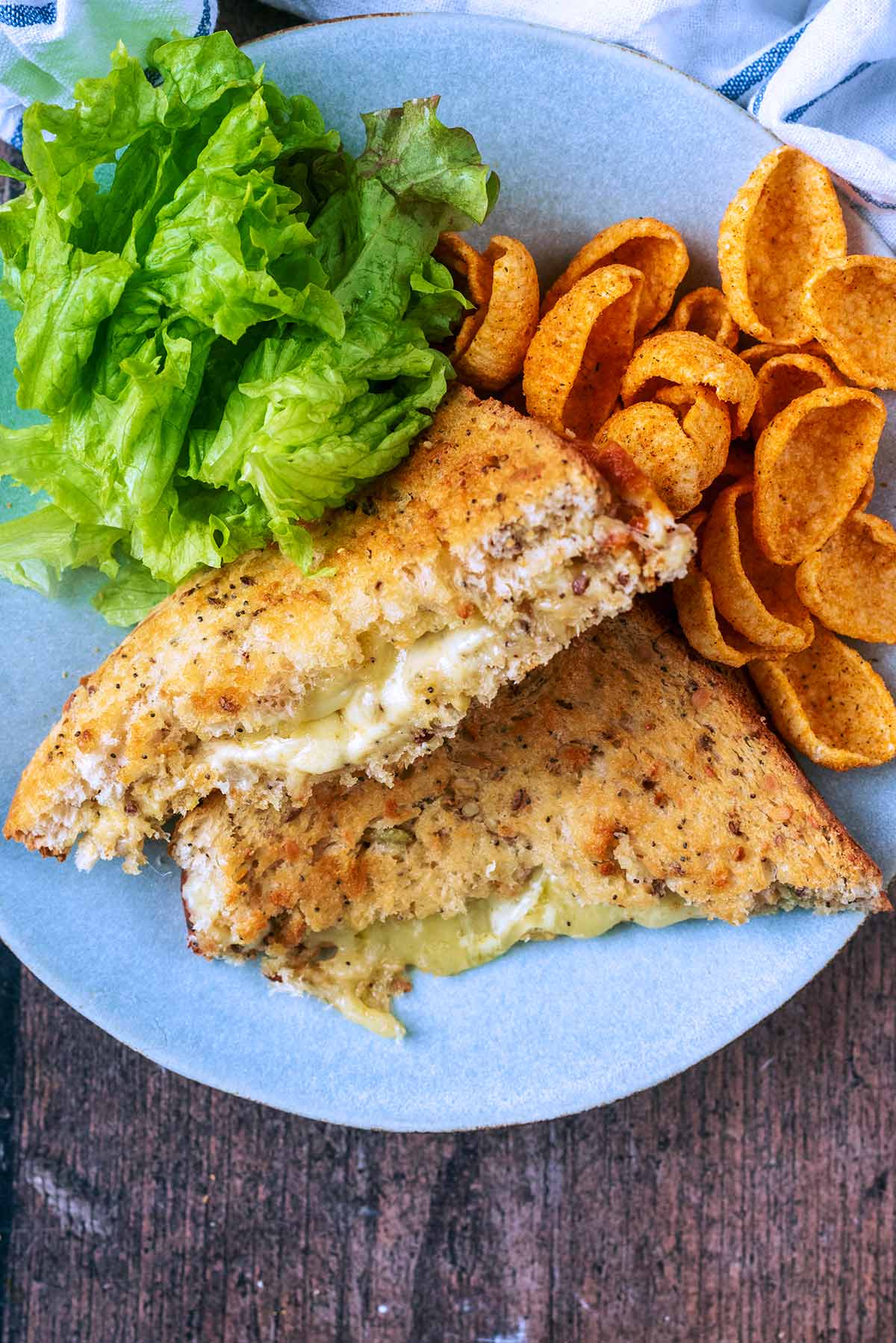A toasted cheese sandwich cut in half on a plate with crisps and lettuce.