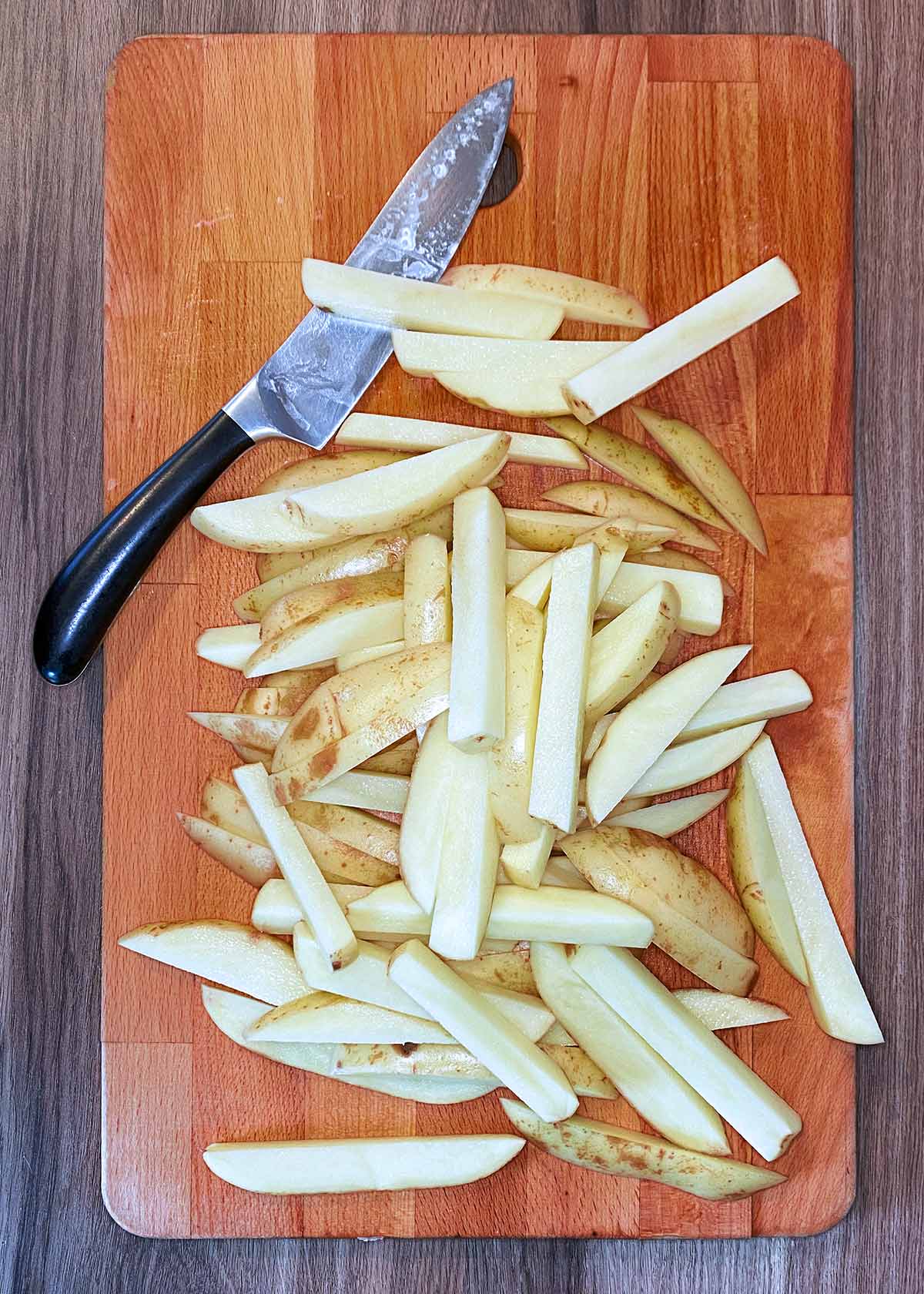 A chopping board with potatoes cut into chips.