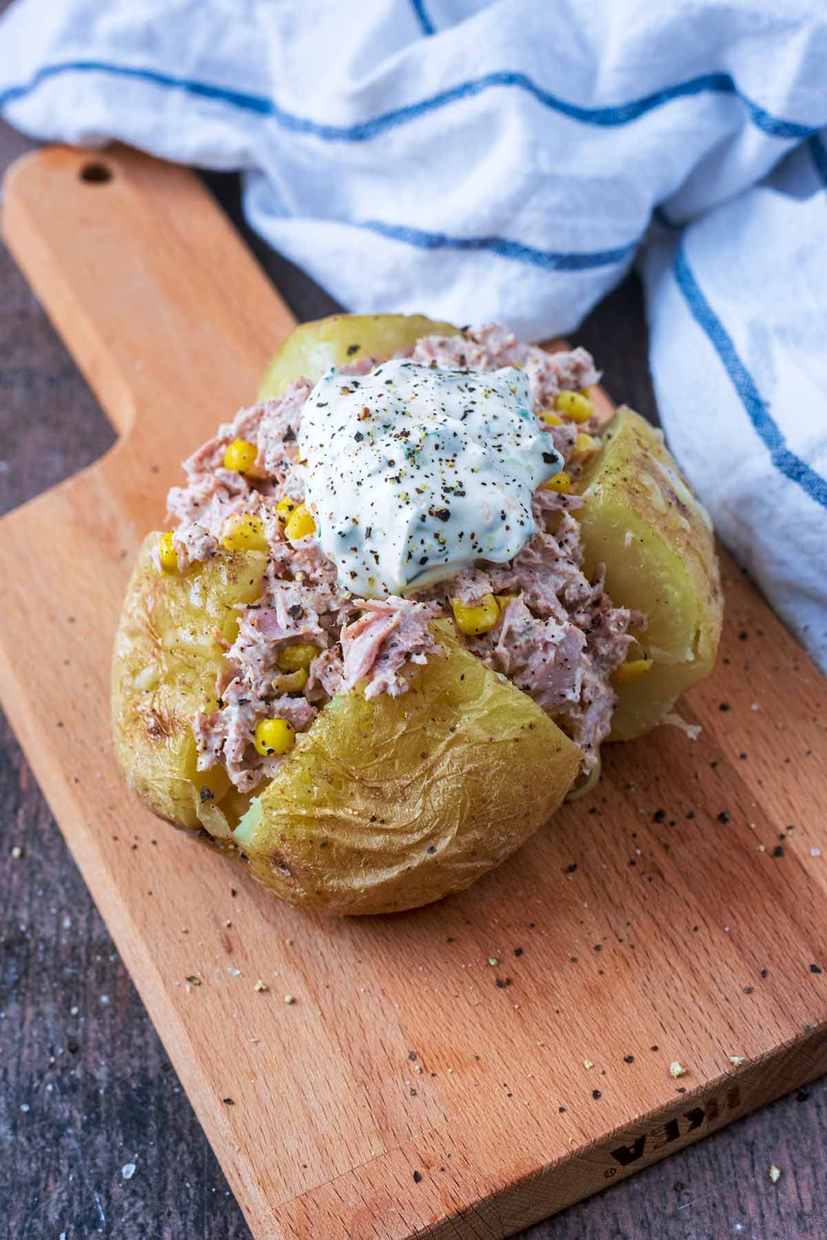 A jacket potato cut open filled with tuna mayo and topped with sour cream.