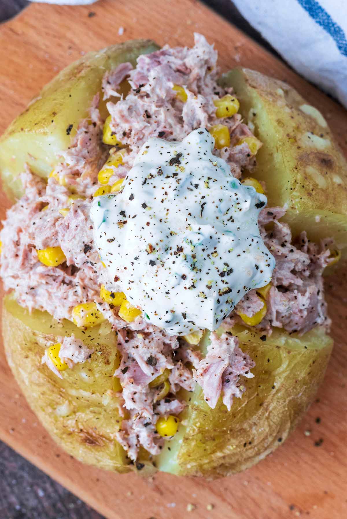 A dollop of sour cream on top of a tuna mayonnaise filled baked potato.