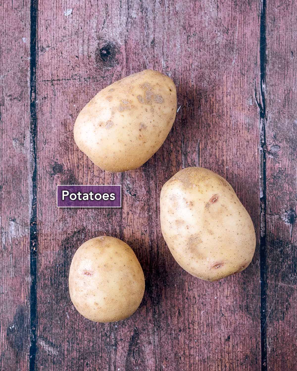 Three potatoes on a wooden surface with a text overlay label.