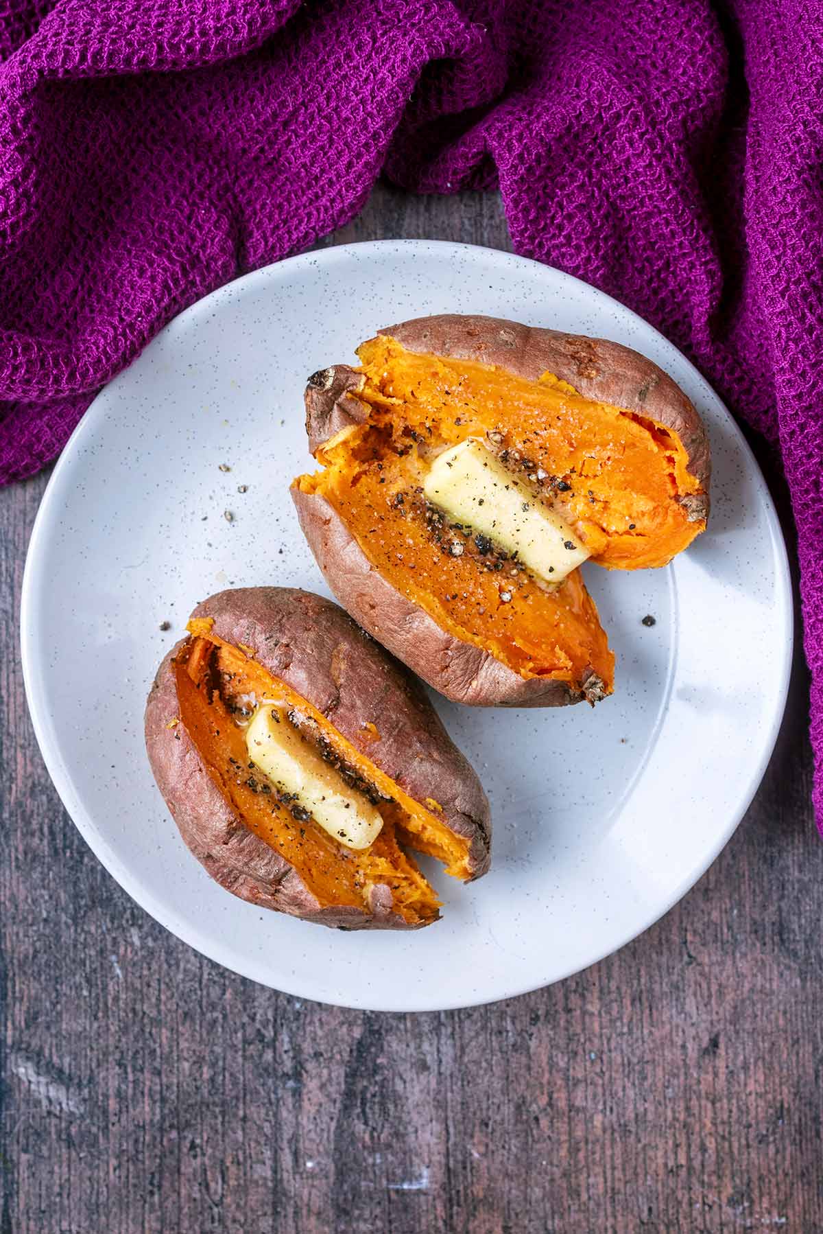 Two cooked sweet potatoes on a plate next to a purple towel.