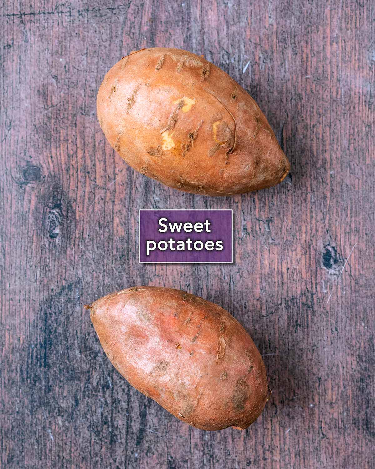 Two sweet potatoes on a wooden surface with a text label overlay.