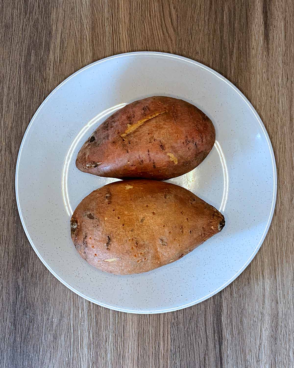 Two pricked sweet potatoes on a plate.
