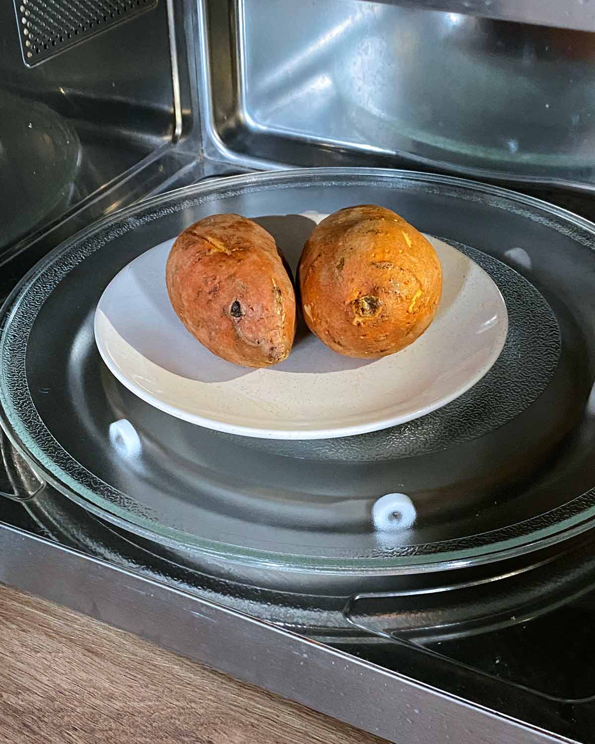 Two sweet potatoes on a plate in a microwave.