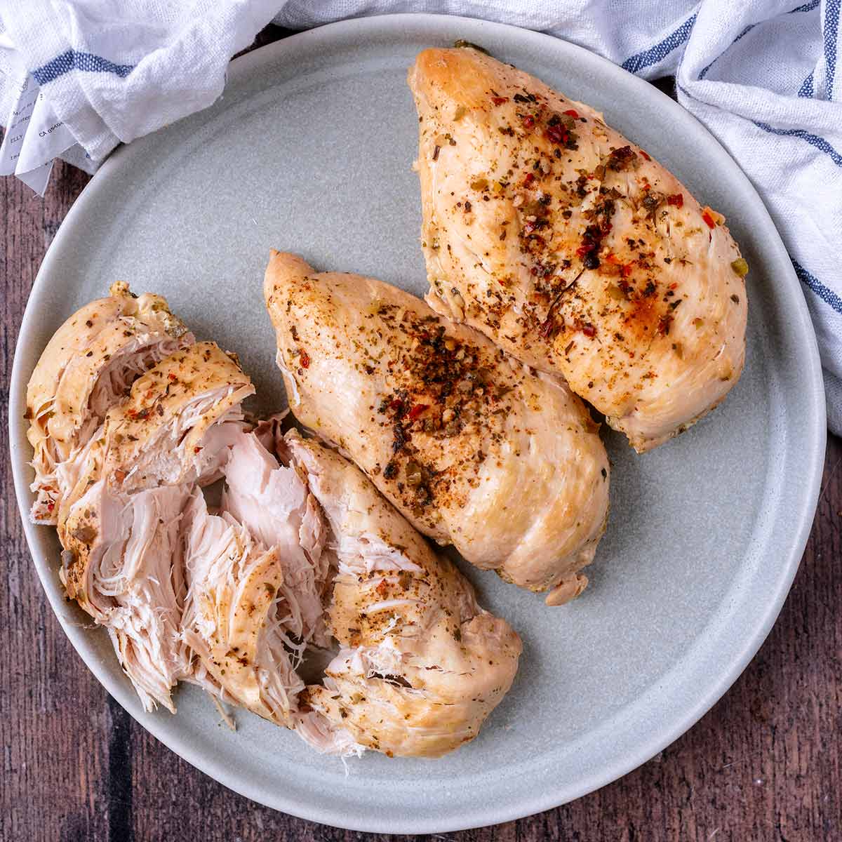 Three slow cooker chicken breasts on a plate, one is sliced.