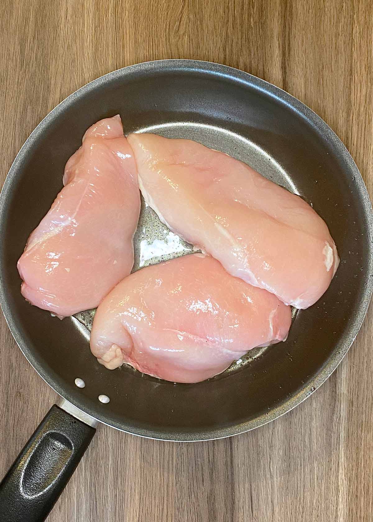A frying pan with chicken breasts cooking in it.